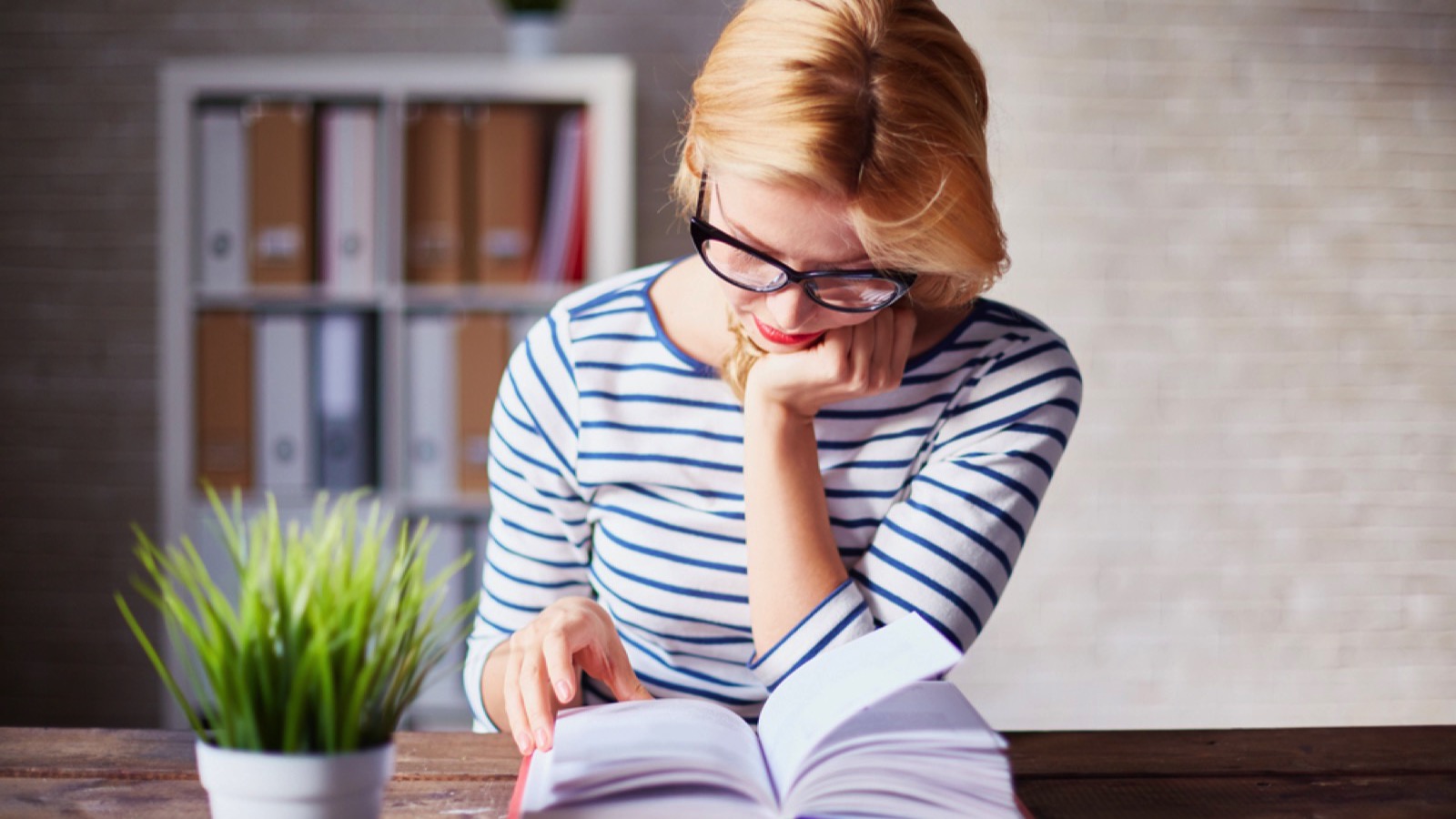 Charming girl sitting by wooden table and reading book