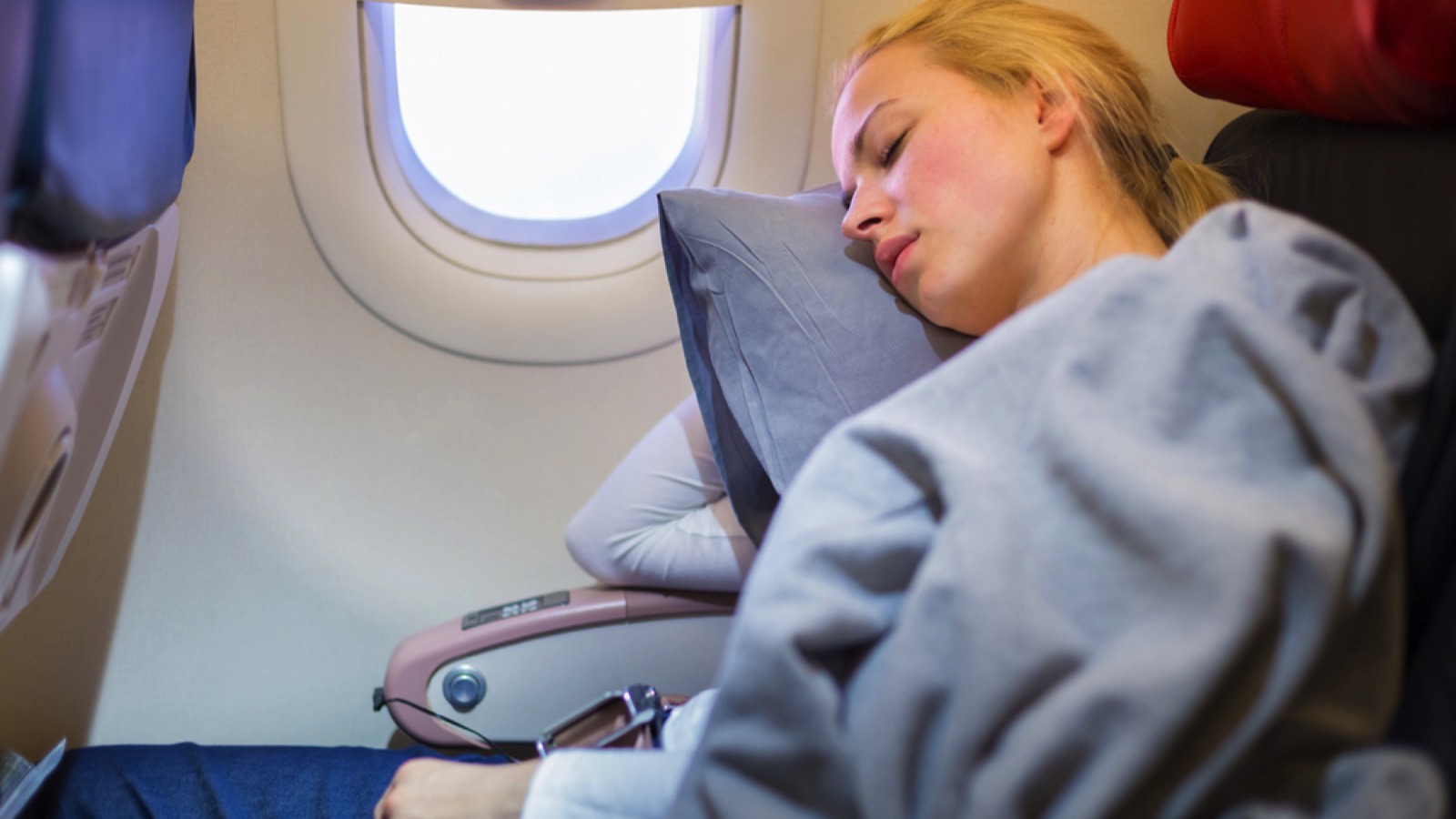 Woman sleeping on window seat with pillow in flight