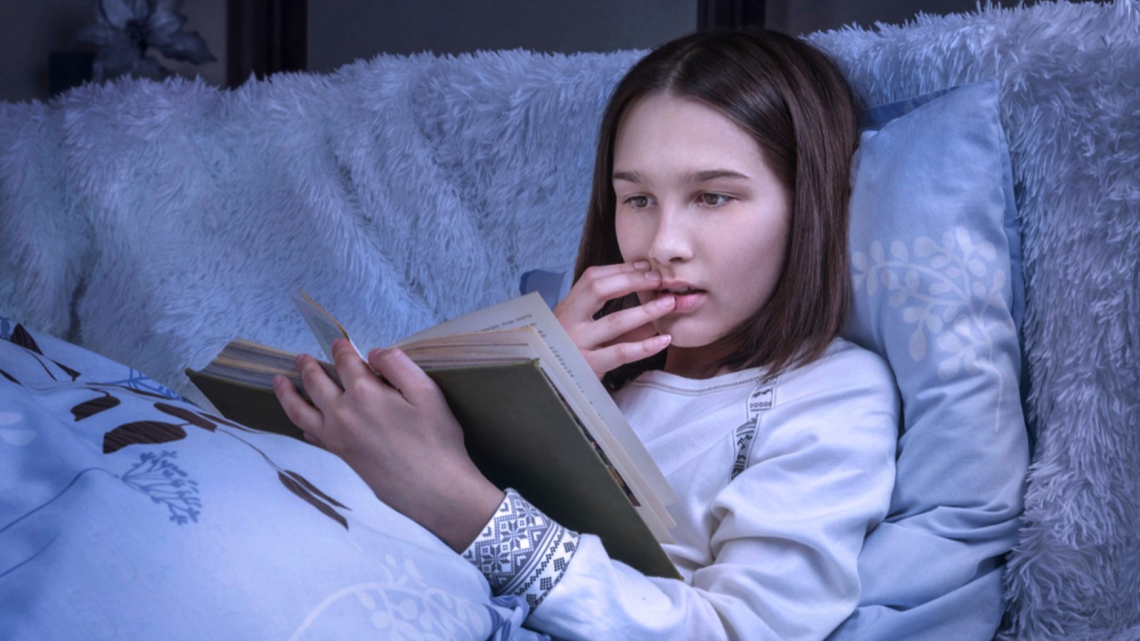 Teen girl reading novel at night