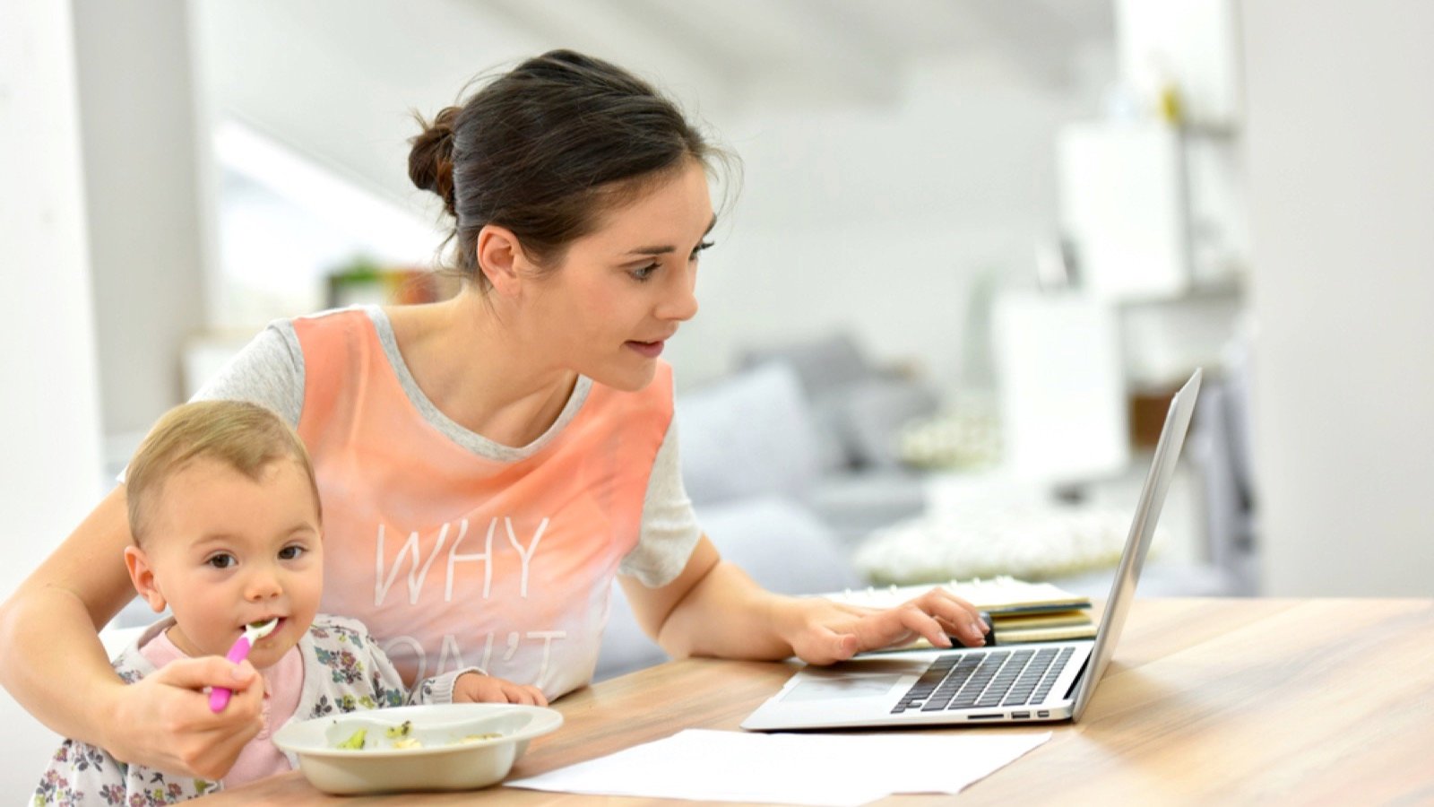 Woman working at home and feeding toddler