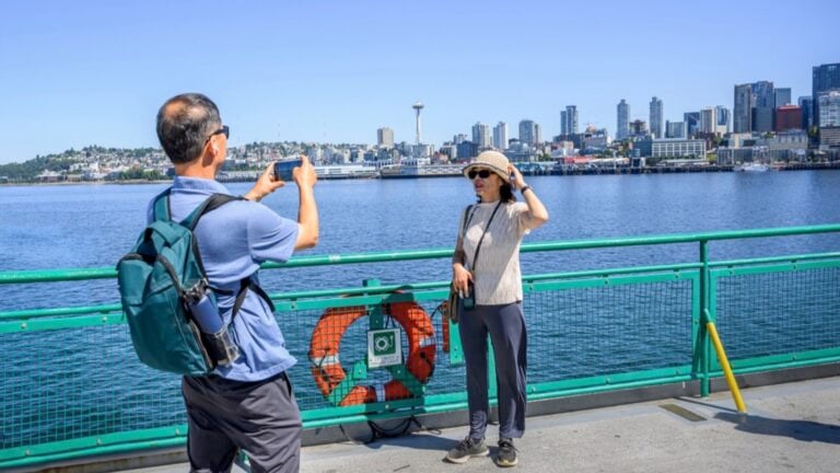 Tourists taking photos using smartphone on the ferry at Elliott Bay. Seattle skyline and the historic Space Needle in the background. Seattle. Washington State.
