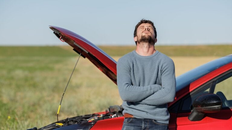 Annoyed young man waiting for assistance after his car broke down.
