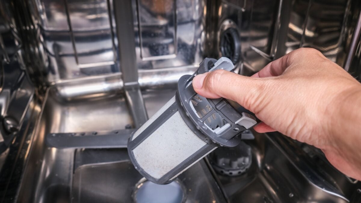 A hand taking out dishwasher filter to clean it.