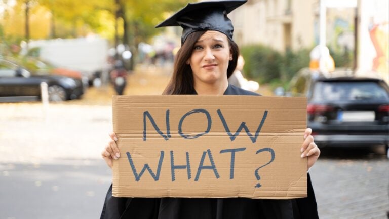 Sad Graduate Student Standing With Now What Placard On Street