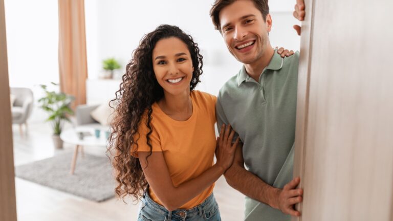 Happy young couple inviting guests in to view their home.