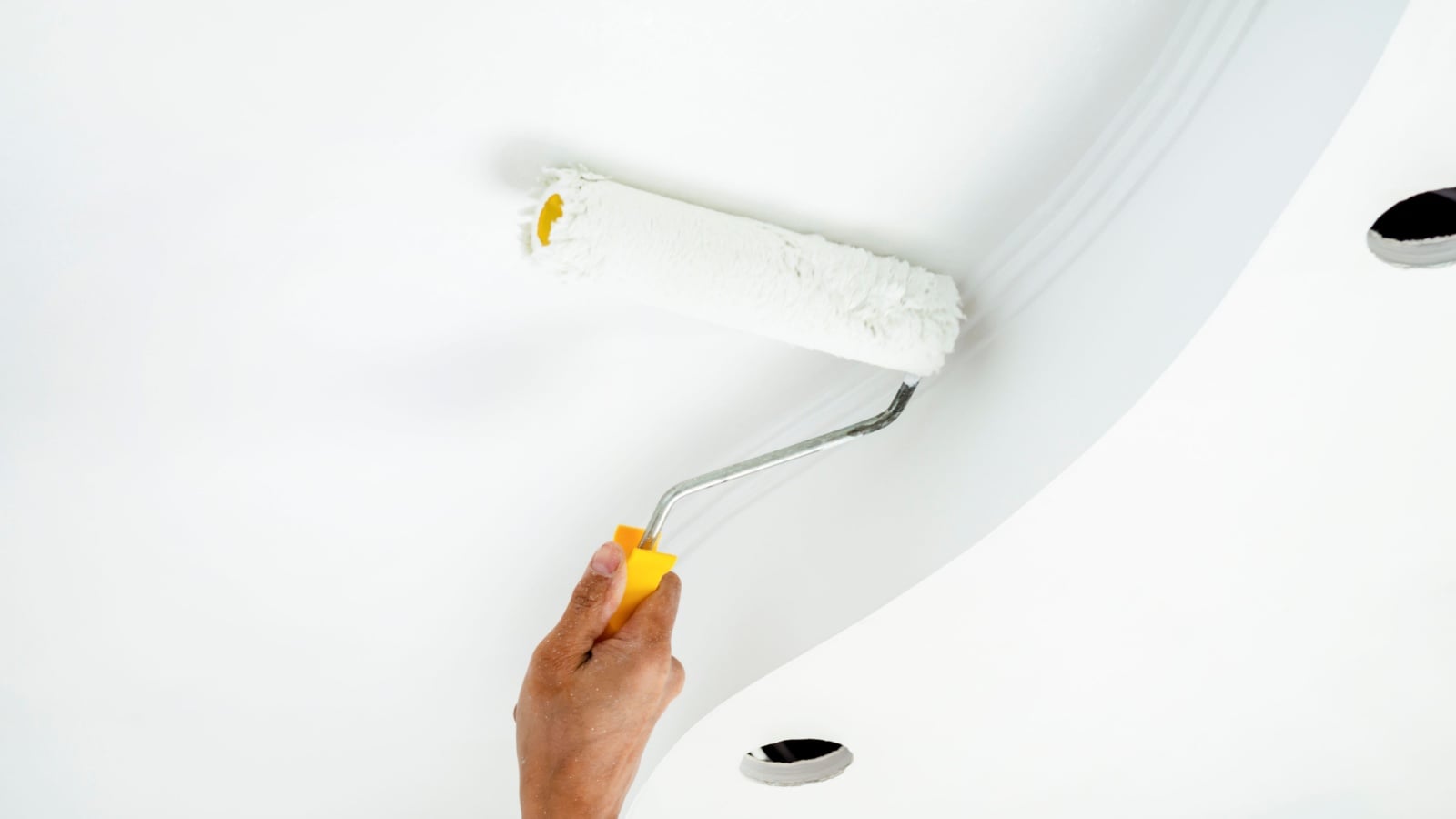 A hand with a roller paints the ceiling white.
