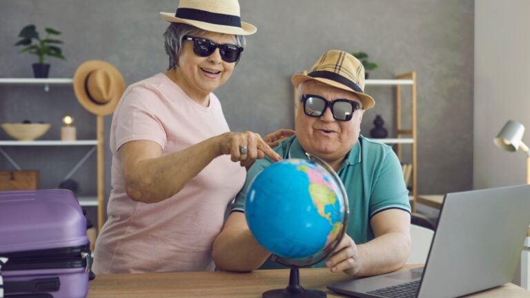 Retired couple pointing on world globe to emigration destination.