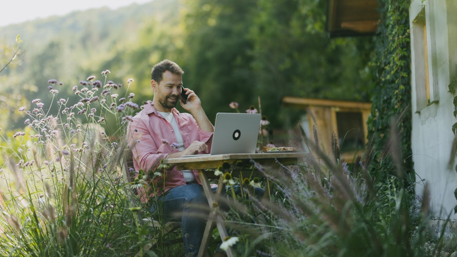 Man working in the garden on laptop, phone calling. Businessman working remotely from outdoor home office.