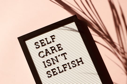 Mindfulness Letter board displaying 'Self Care Isn't Selfish' with artistic shadow on pink background.