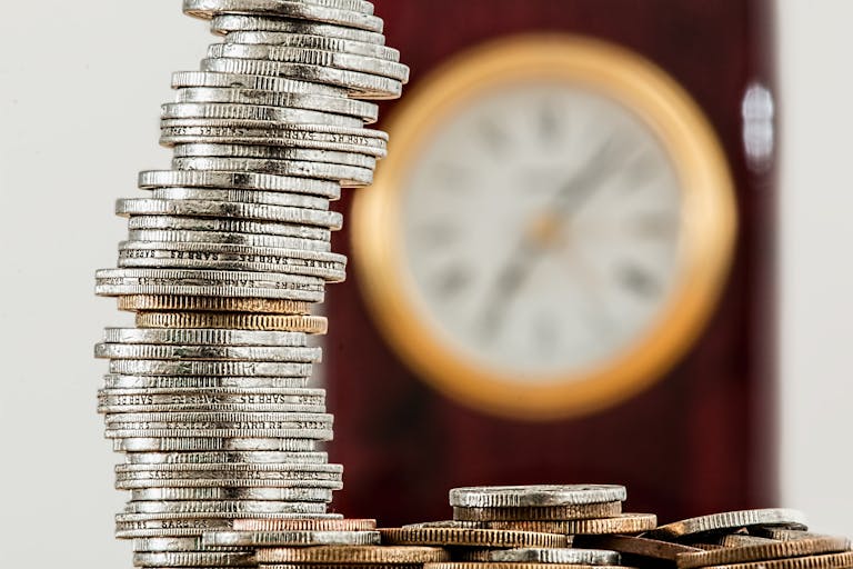 Time A close-up image of stacked coins with a blurred clock, symbolizing time and money relationship.