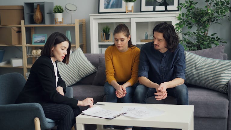Affordable Housing Couple discussing property with real estate agent in cozy living room setting, reviewing documents.
