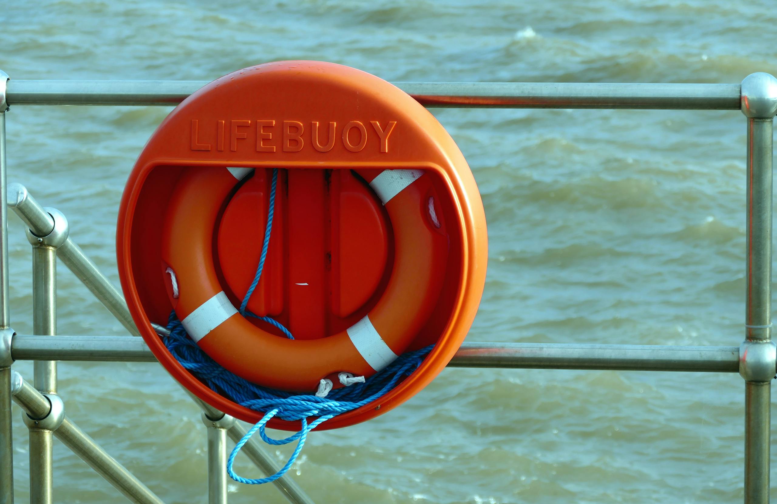 Emergency Fund A bright orange lifebuoy hangs on a metal railing overlooking the sea, signifying safety at the coast.