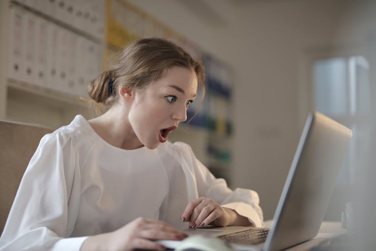 How to Pay Off Student Loans Fast Surprised woman sitting at desk with laptop indoors, expressing amazement.