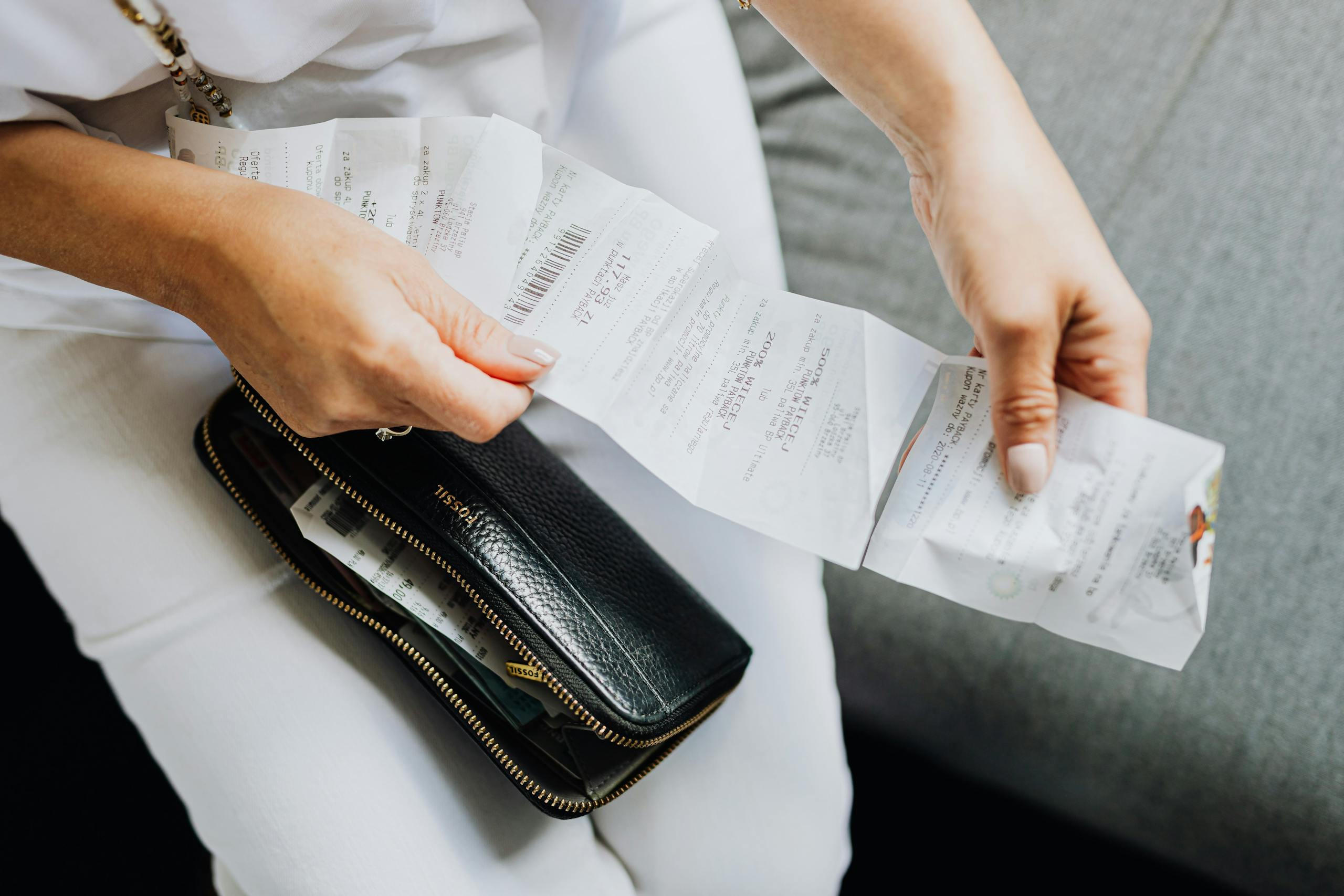 Grocery Cost Close-up of a woman's hands managing multiple receipts taken from a black wallet.