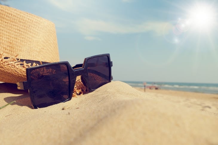 Summer Travel Close-up of sunglasses and straw hat on sandy beach under bright sunlight, perfect summer vibe.