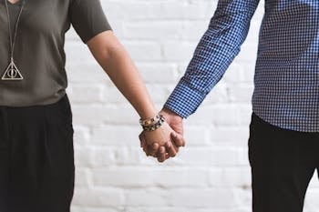 Financial Infidelity Close-up of a couple holding hands in casual fashion attire against a white brick wall.