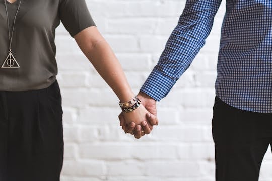 Financial Infidelity Close-up of a couple holding hands in casual fashion attire against a white brick wall.