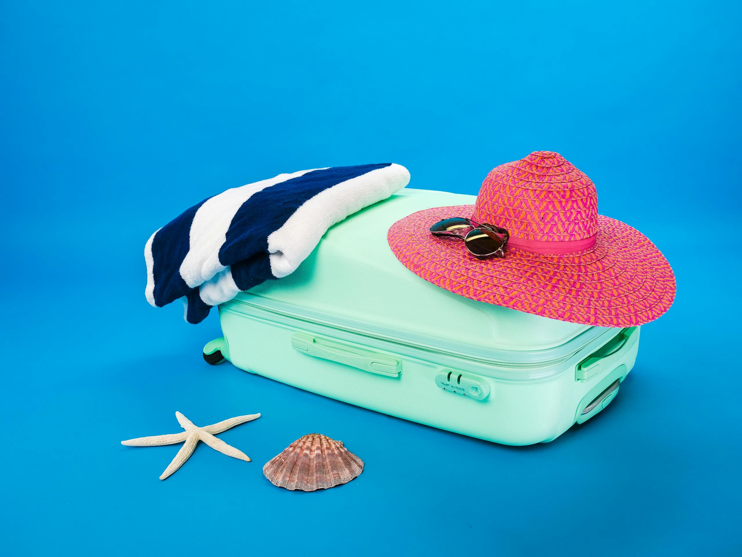 Summer Travel Beach essentials including a suitcase, hat, towel, and seashells on a bright background.