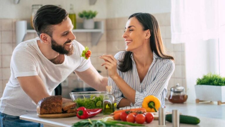 Couples in kitchen feeding each other.