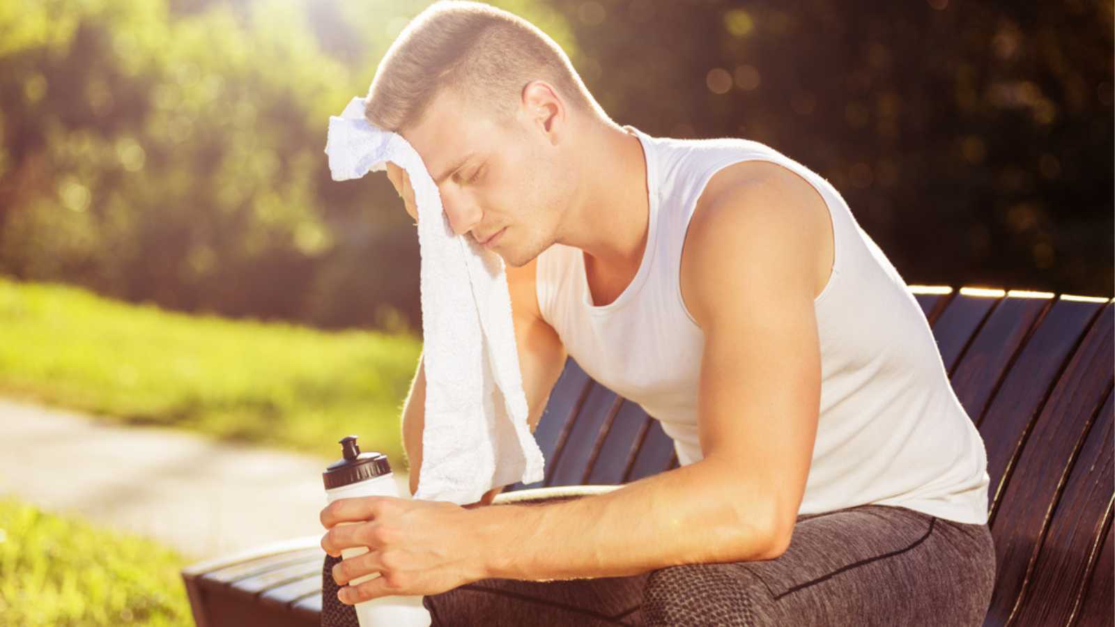 Exhausted male after exercise drinking water and wiping sweat with towel.Tired man resting from sport training Image is intentionally toned.
