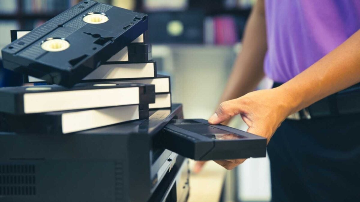 Close-up hand chooses and put or insert video cassette tape VHS old retro style on video record playback concept of vintage electric and electronic appliances multimedia player device old fashioned.