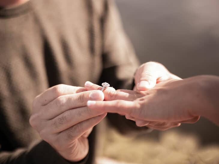 Man placing an engagement ring on woman's finger during proposal.