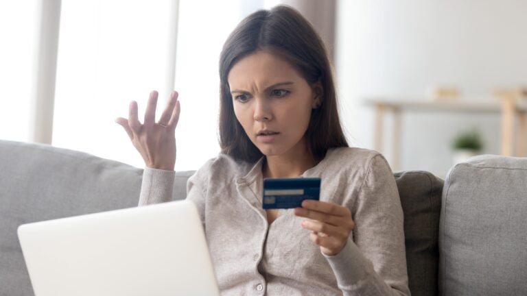 How to pay off credit card debt: Woman holding credit card with a stunned look on her face looking at laptop
