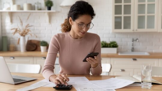 Happy young Caucasian woman sit at desk at home manage household expenses