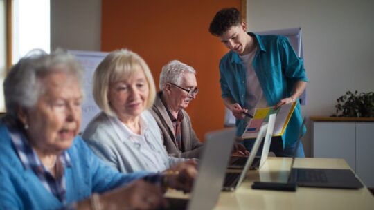 Senior group in retirement home with young instructor learning together in computer class
