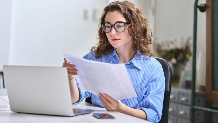 Young busy business woman manager, lawyer or company employee holding accounting bookkeeping documents checking financial data or marketing report working in office with laptop. Paperwork management