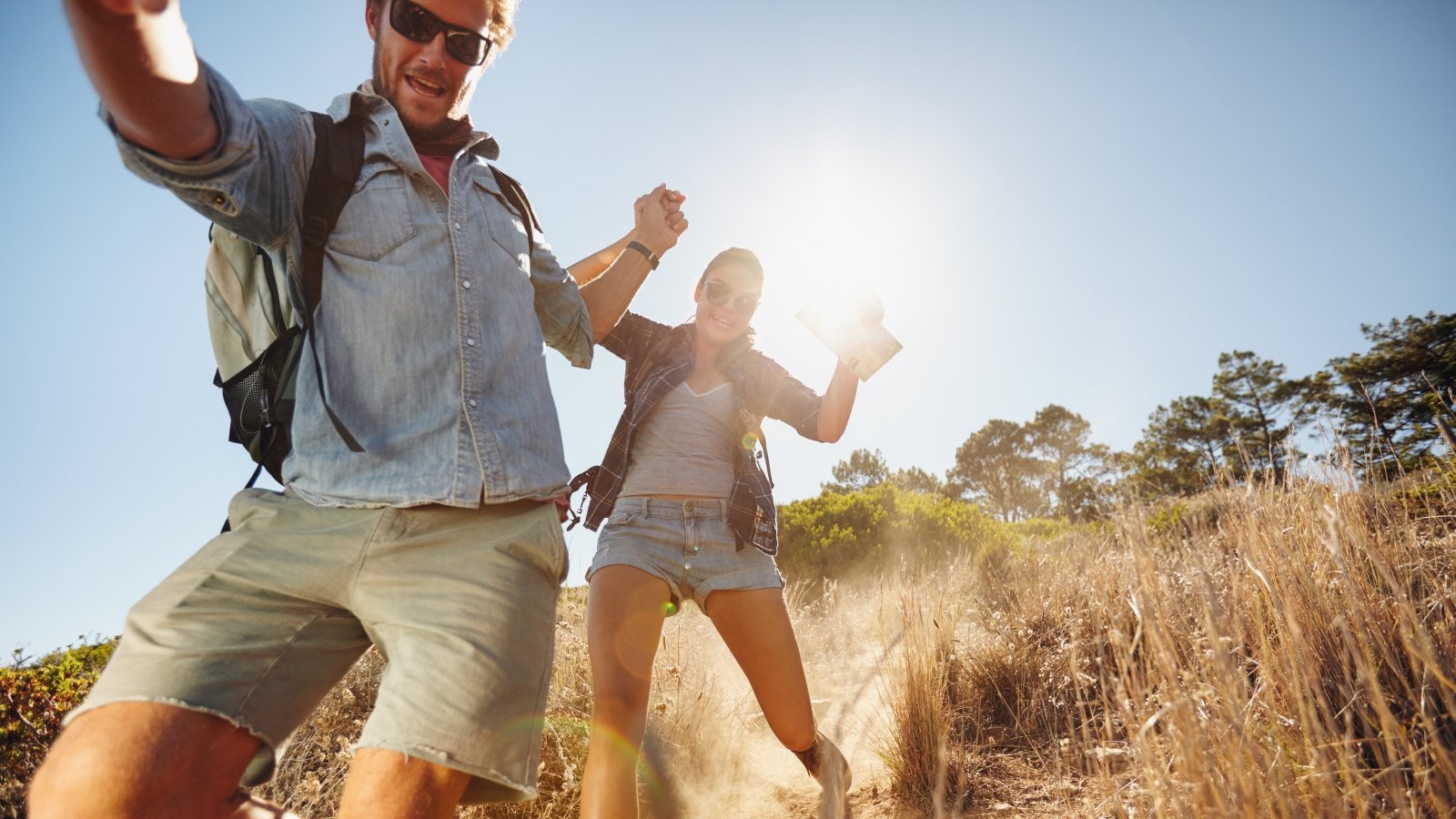 Portrait of happy young couple having fun on their hiking trip, sliding down the mountain trail. Caucasian hiker couple enjoying themselves on summer vacation.