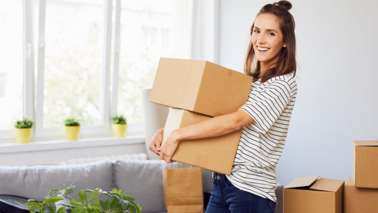 Young woman moving into new apartment holding cardboard boxes with belongings